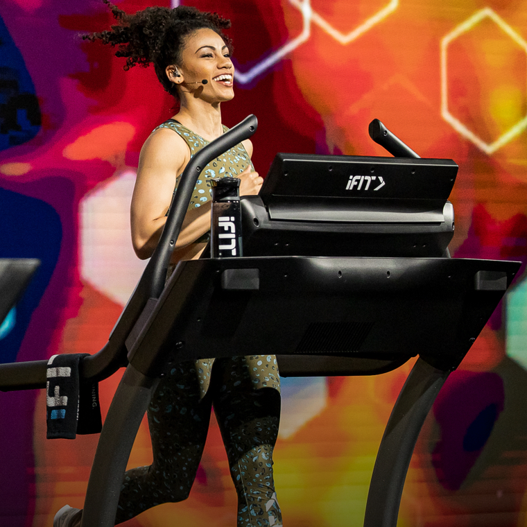 iFit Trainer Smiling while jogging on treadmill and giving Live & On-Demand Studio Classes