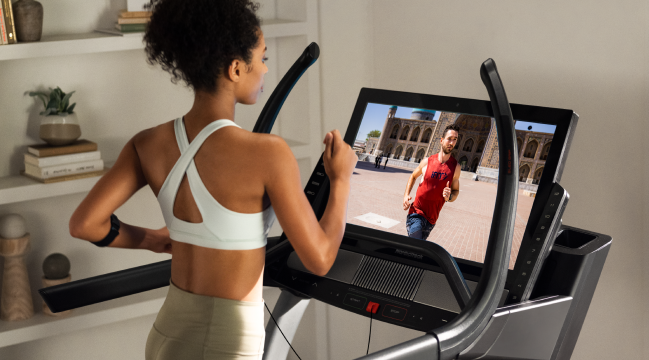 woman running on her nordictrack incline trainer and looking at the hd touchscreen